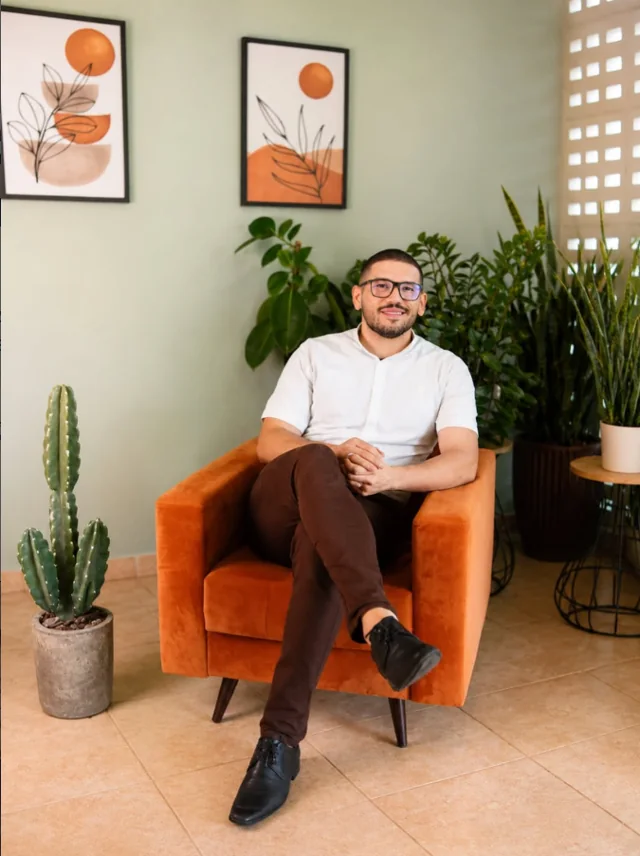 Lucas Mattos sentado em uma poltrona, em um ambiente com plantas